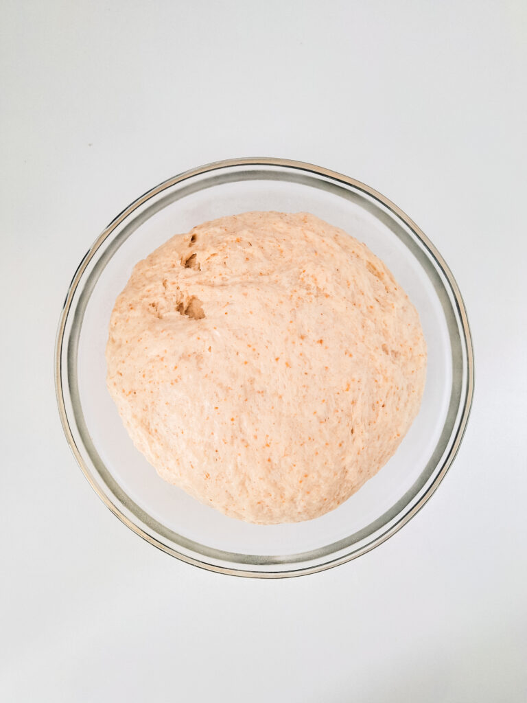 clear bowl on white background with sourdough dough in it
