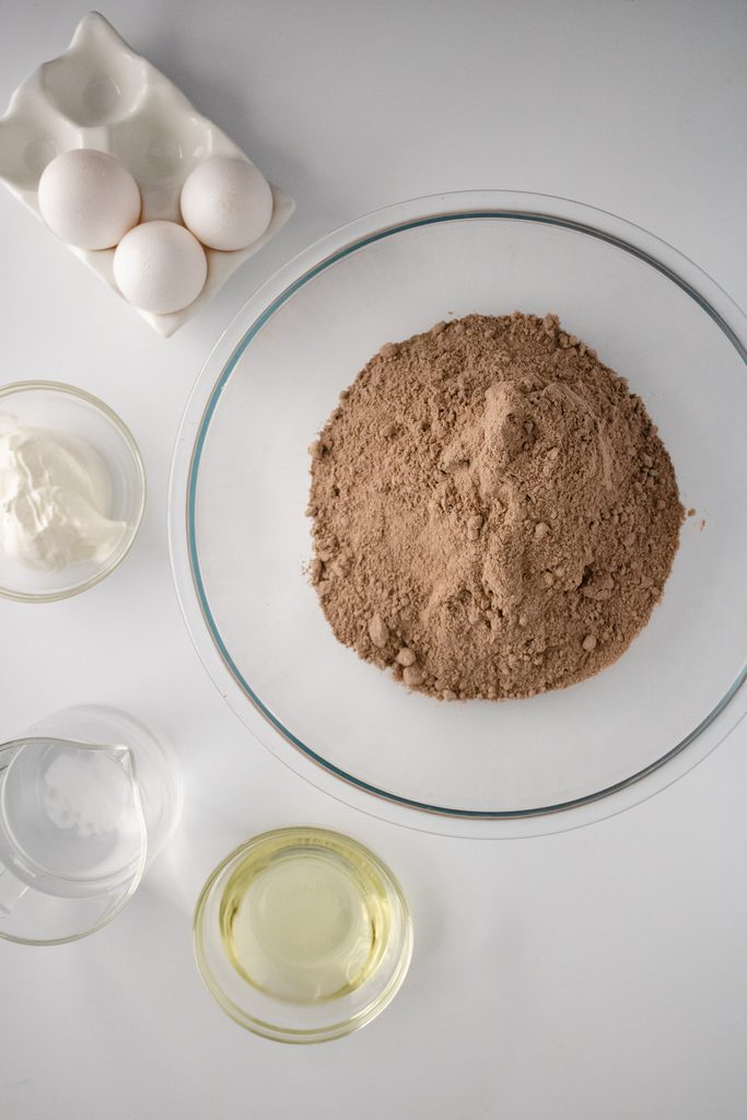 Ingredients for an enhanced chocolate cake mix arranged around a mixing bowl