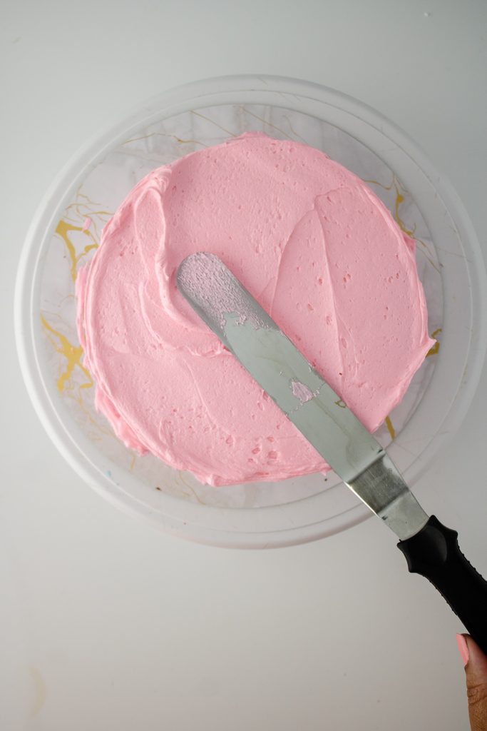 Pink buttercream being spread over a round chocolate cake