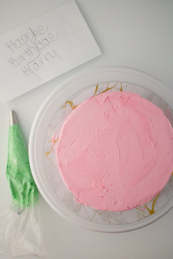 Pink frosted cake prepared for green birthday-message lettering